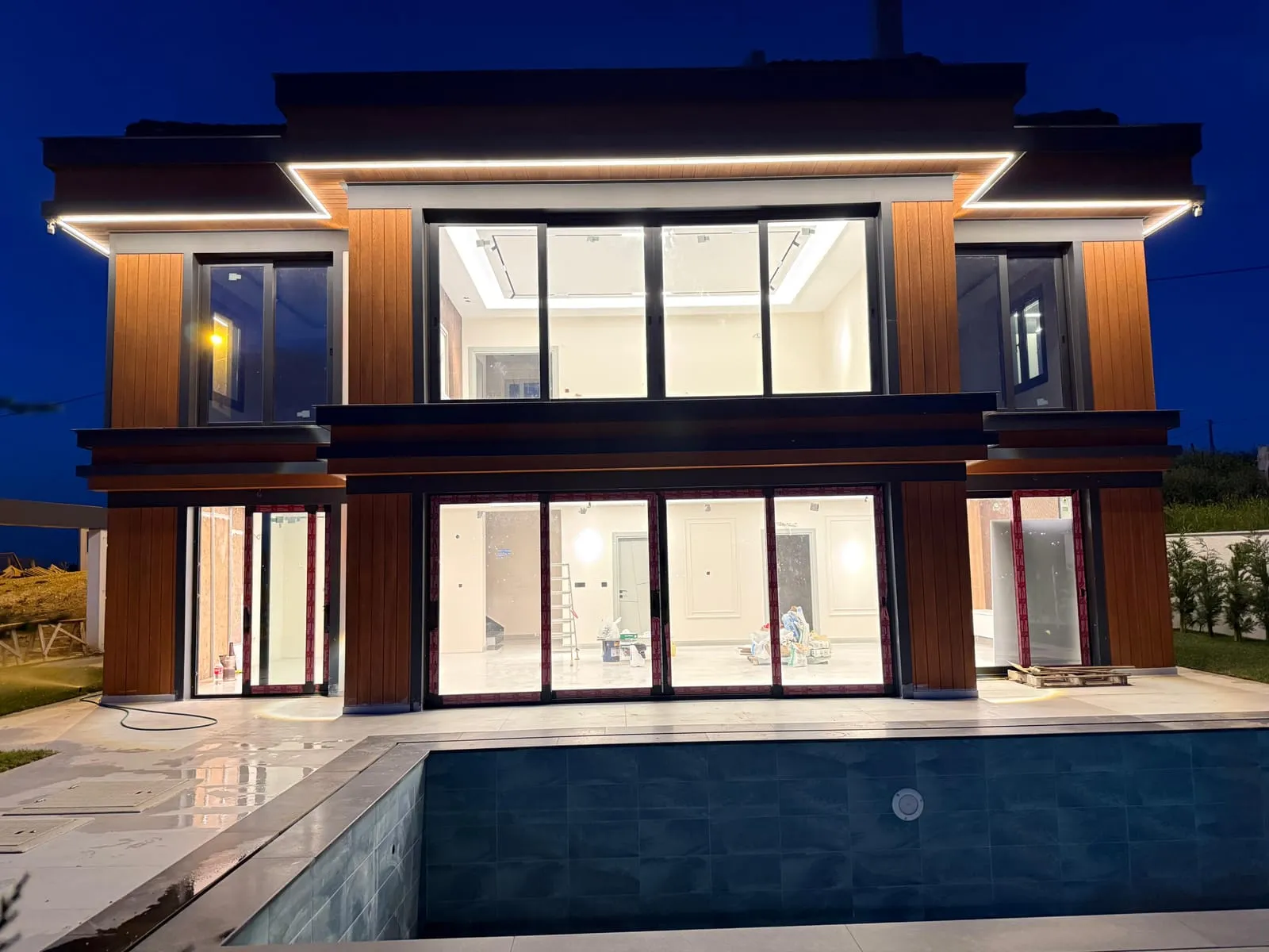 Havuz tarafından villanın gece görünümü: saçak altı LED çizgi ve aydınlatılmış salonlar