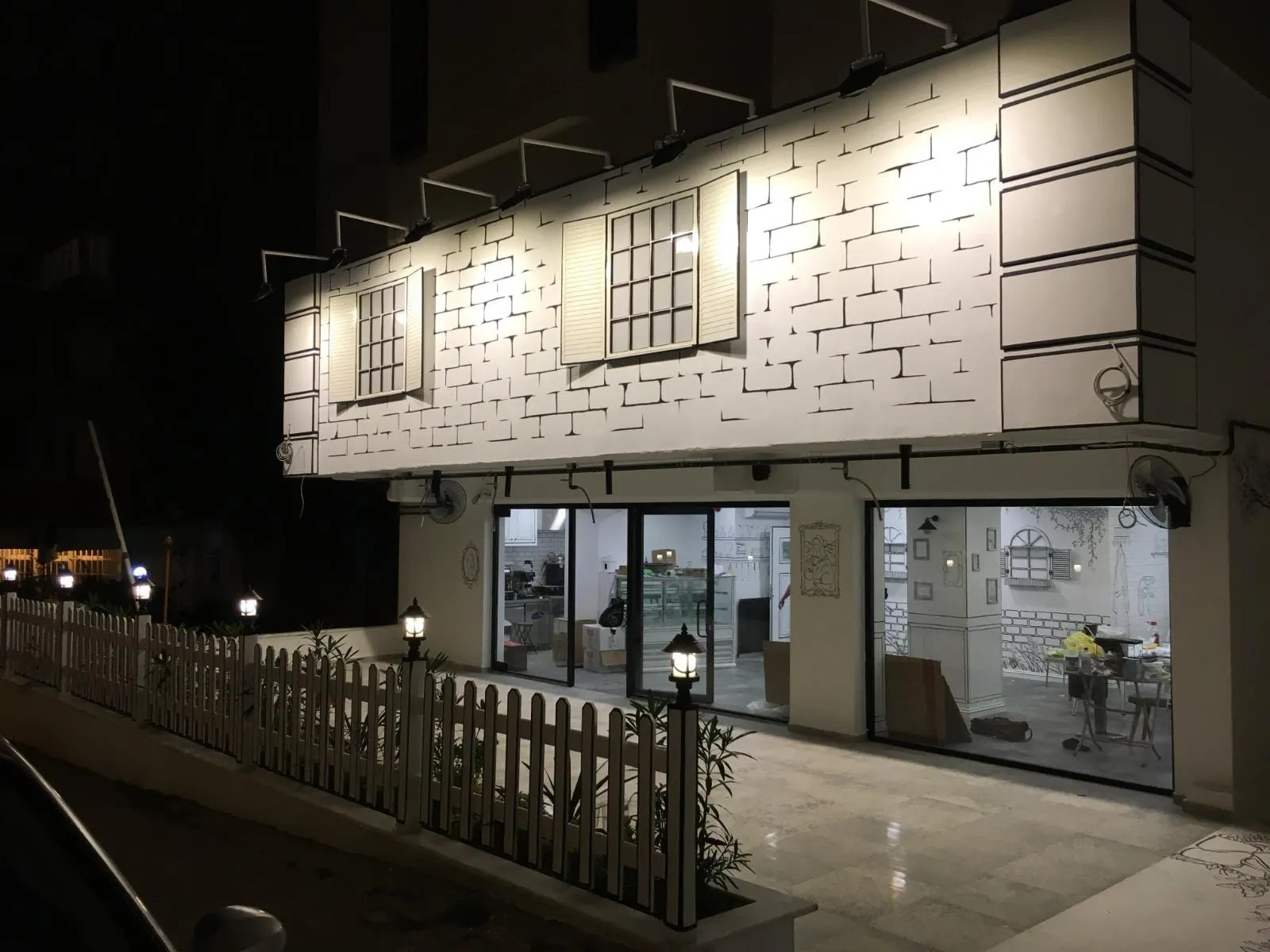 Kafenin gece görünümü: tuğla desenli cephe, cephe aplikleri ve vitrin aydınlatması
