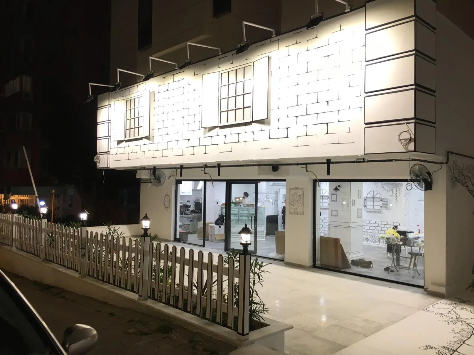 Bahçe çiti üzerindeki fenerler ve kafenin ışıklı vitrini