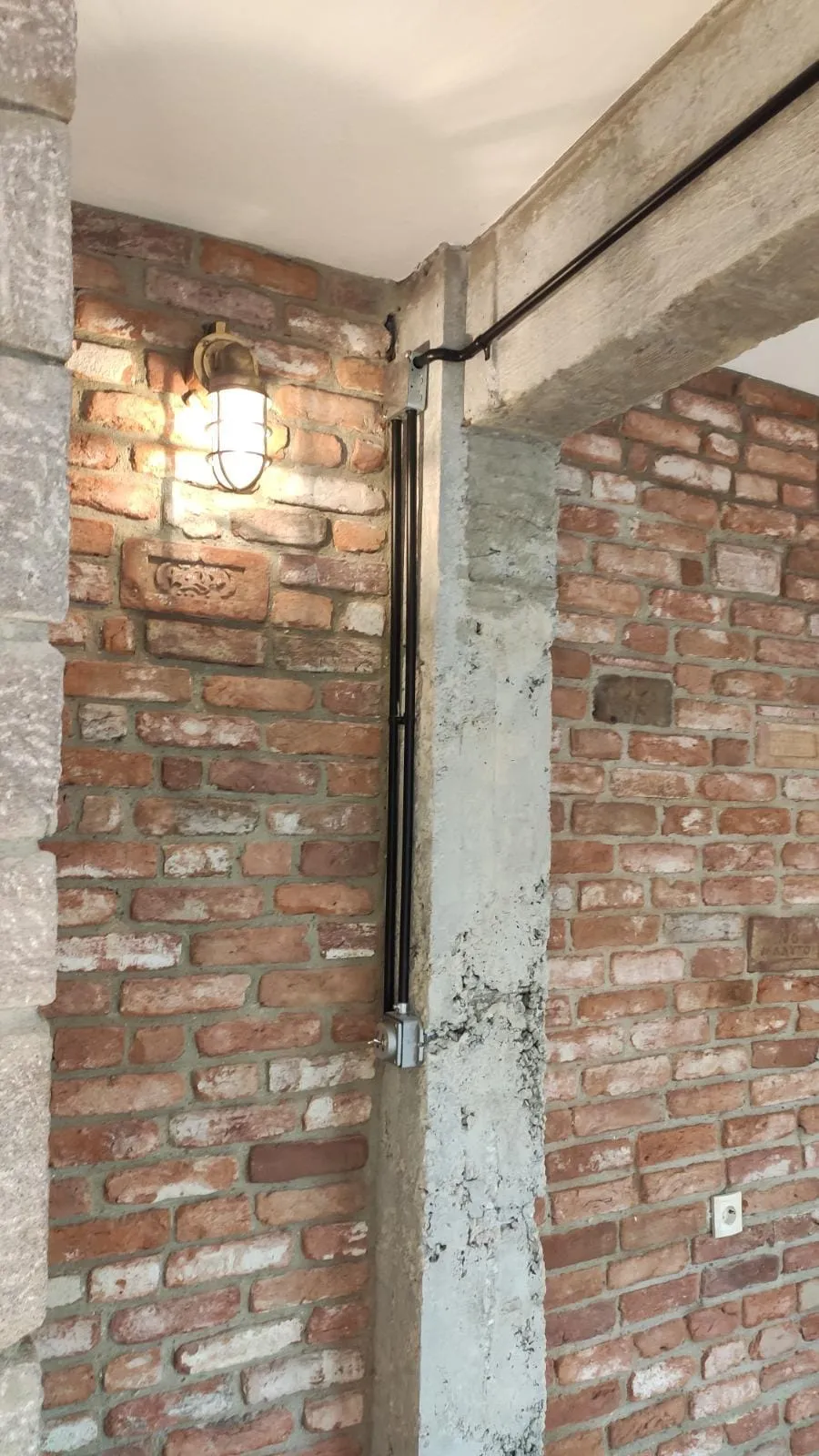 Eski tuğla duvarda siyah boru hattıyla beslenen kafesli aplik