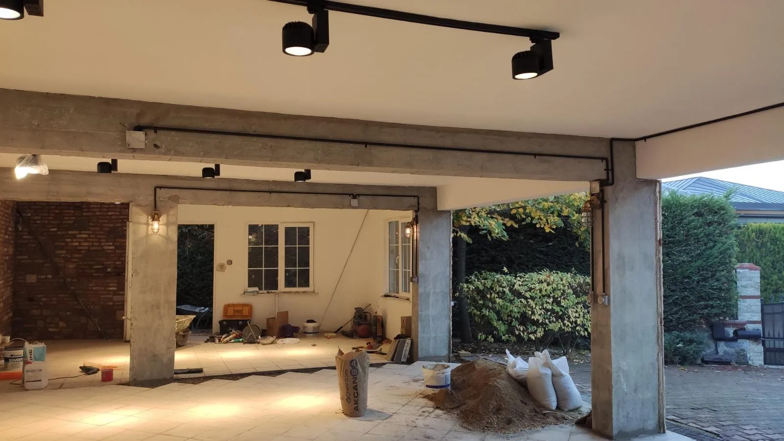 Villanın açık garajında ray spotlar, tuğla duvar ve beton kolonlar