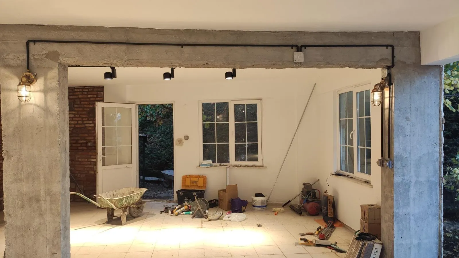 Garajdan villa girişine bakış: siyah boru hatları ve kafesli aplikler